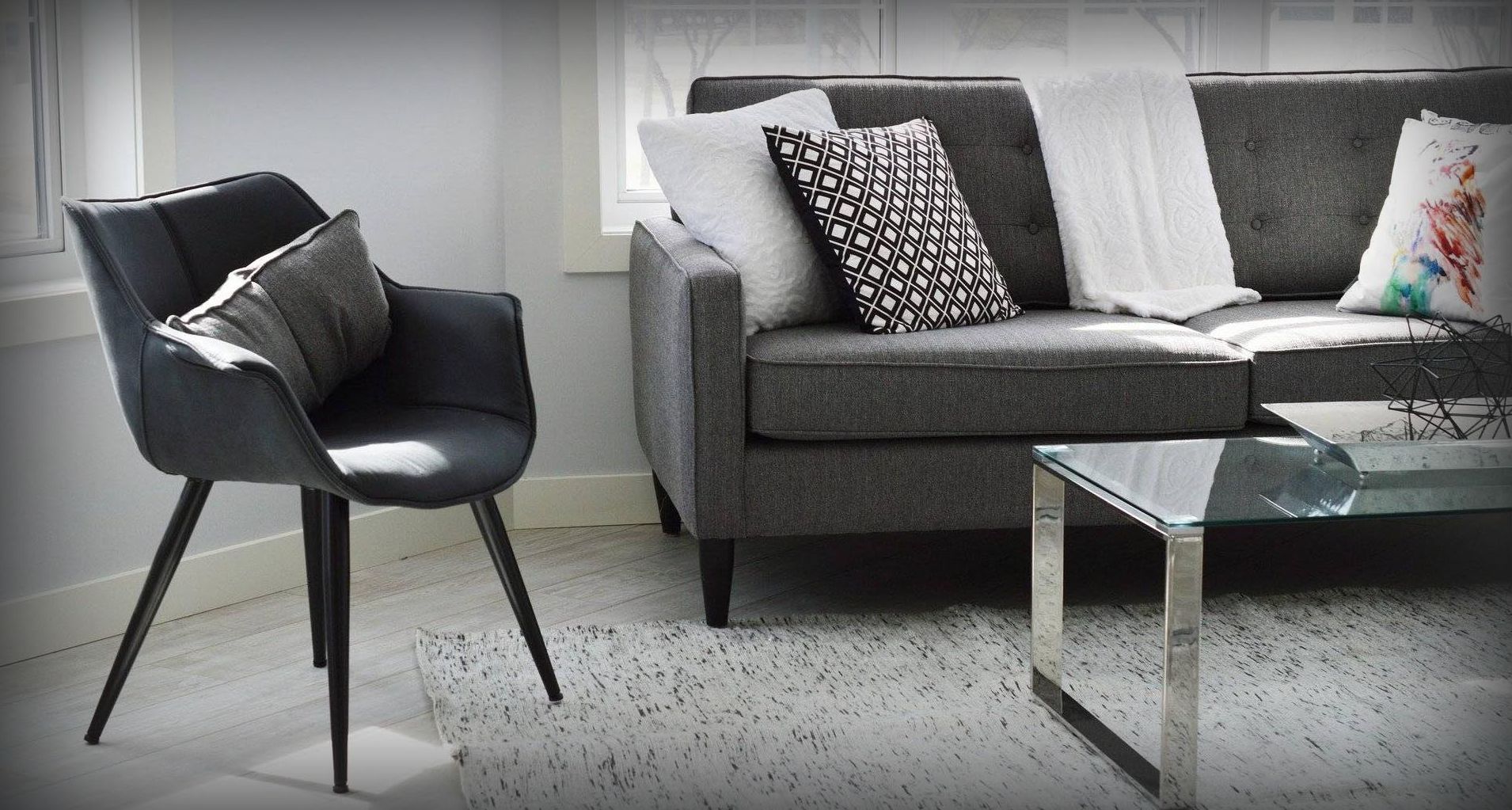 Grå sofa med svart stol og glassbord